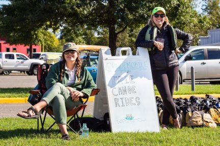 A USFS staff member and outdoor leader on either side of a white sign that says 'free canoe rides'