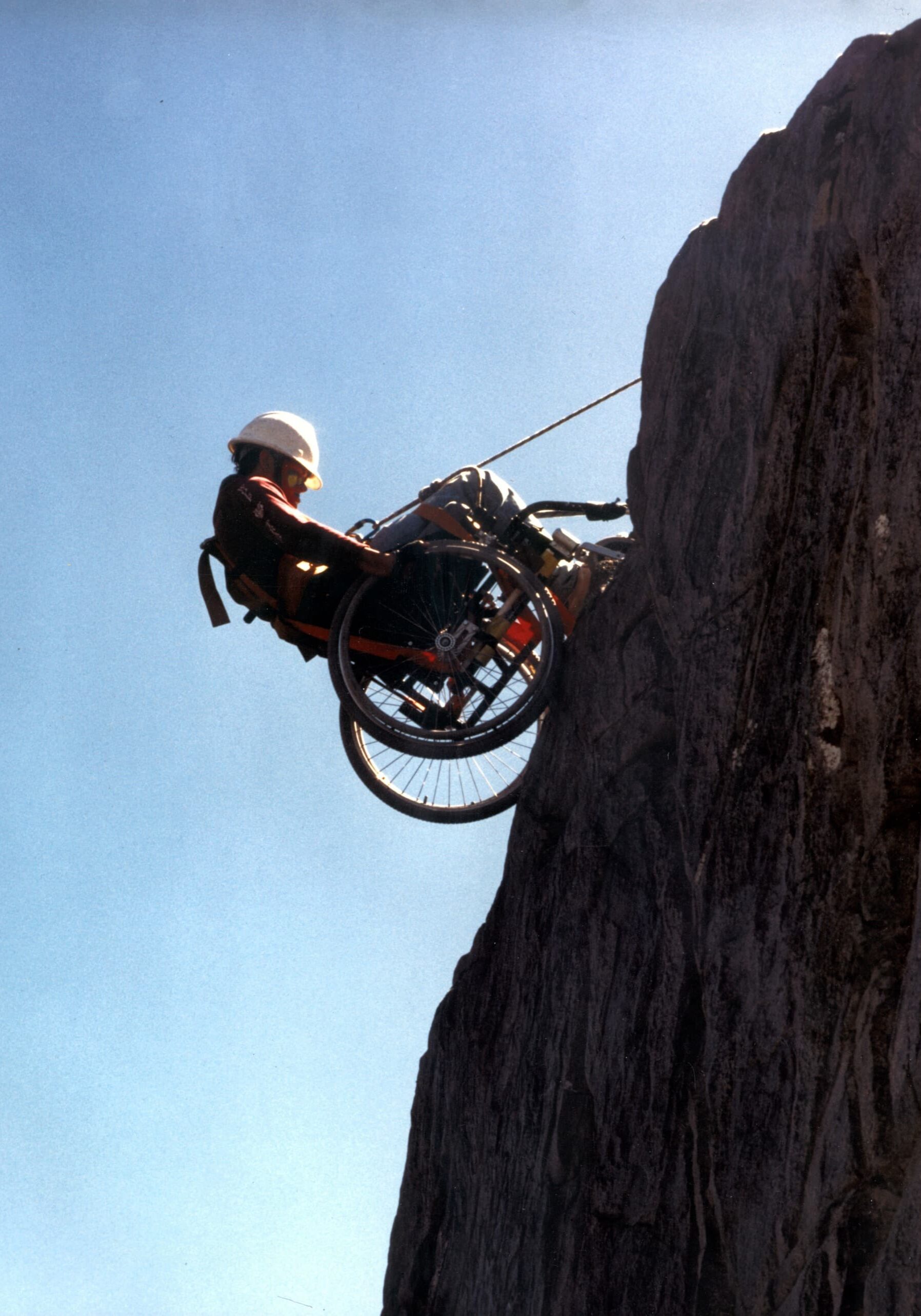 dangling wheelchair Erin Broadbent. The trip included a day of rappelling down a sheer rock face along the river. Erin's eyes lit up with excitement. Greg Lais describes the scene, "I was standing in the river at the base of the cliff, watching these two wheelchair rims edge their way over the cliff. Erin was cool as a cucumber, started rolling her way down the sheer cliff face when I took the picture. A moment later, her wheel caught in a crack of rock and she flipped sideways. I looked up at her and asked if she was nervous. She responded, 'Nah, I already broke my neck once, this is no big deal.'" Peering at Erin over the cliff, the crowd above burst into applause as Erin freed herself and made her way down the cliff. After Erin, everyone in the group enthusiastically rappelled down the cliff.